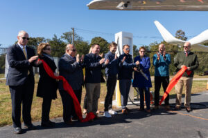 Dignitaries cut a ceremonial ribbon celebrating the commissioning of Shoreline Aviation’s new BETA Technologies-designed electric aircraft charging station, at Marshfield Municipal Airport.