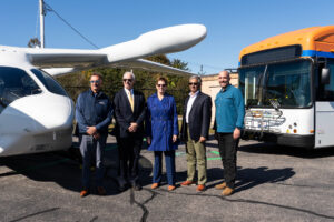Shoreline Aviation President Keith Douglass, left, MassDOT Aeronautics Administrator Jeff DeCarlo, FAA Regional Administrator Colleen D'Alessandro, Eversource VP of Energy Efficiency and Electric Mobility at Eversource Tilak Subrahmanian, and BETA Technologies COO Blain Newton pose with BETA’s ALIA 250 and GATRA’s all electric bus. Photo courtesy of BETA Technologies