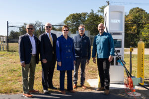Eversource VP of Energy Efficiency and Electric Mobility Tilak Subrahmanian, left, MassDOT Aeronautics Administrator Jeff DeCarlo, FAA Regional Administrator Colleen D'Alessandro, Shoreline Aviation President Keith Douglass, and BETA Technologies COO Blain Newton pose with BETA’s Level 3 fast charger at Marshfield Municipal Airport. Photo courtesy of BETA Technologies
