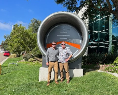Shoreline Aviation pilot Ryan Merriam and Director of Operations P.J. Flanagan stand behind a large turbine engine intake section during their visit to LOFT.