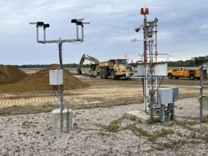 An excavator and dump truck are framed by sophisticated airport electronics. 